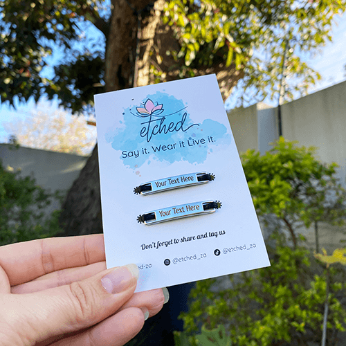 Image of etched product card showing shoe tags with Your Text Here on them being held up by a hand with a tree in the background