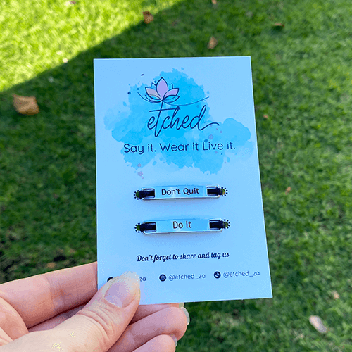 Image of etched product card showing the Don't quit Do It shoe tags being held up by a hand with a grass background