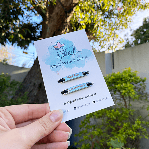 Image of etched product card showing the First Run Then Champagne shoe tags being held up by a hand with a tree in the background