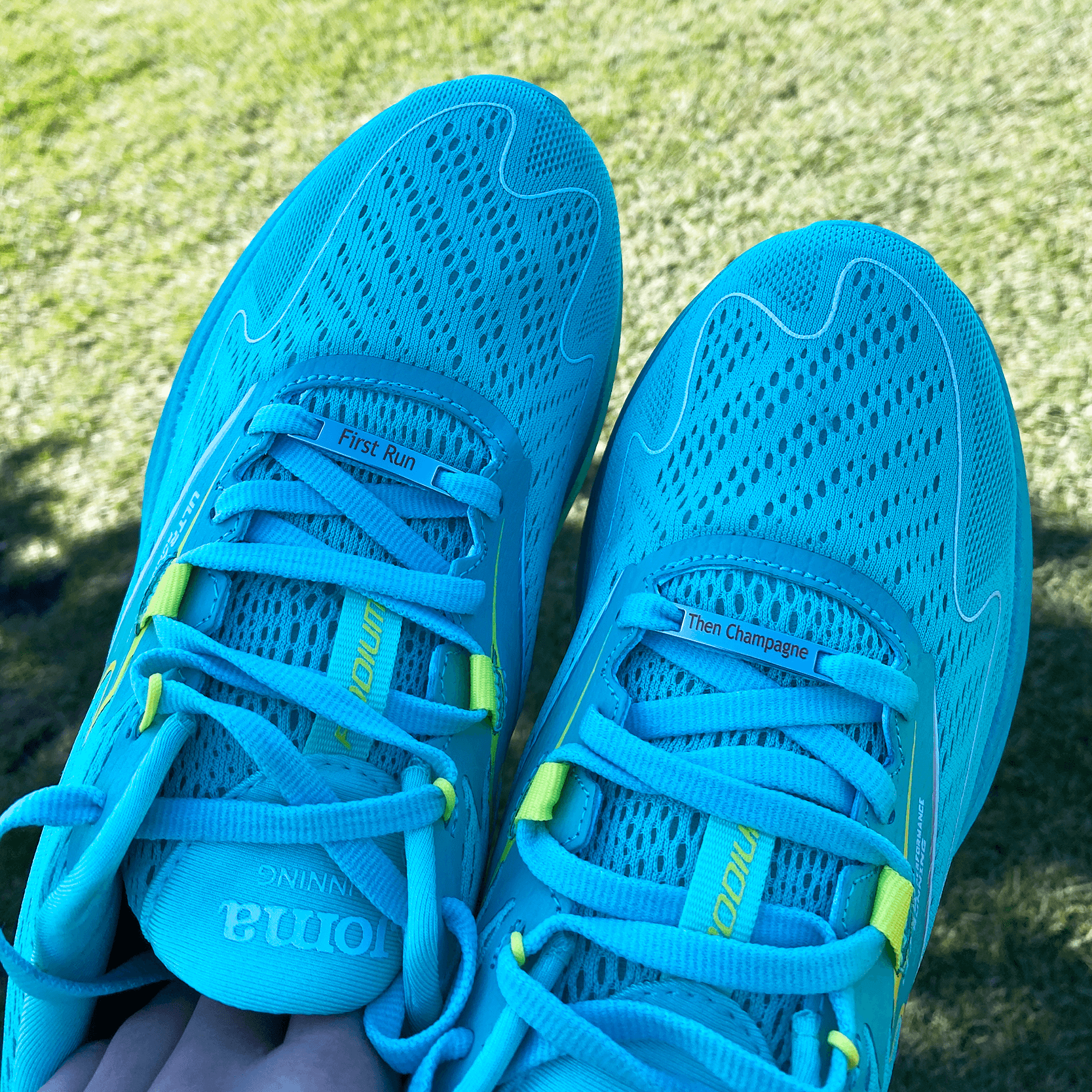 Image of etched shoe tags First Run Then Champagne on a pair of running held up at an angle