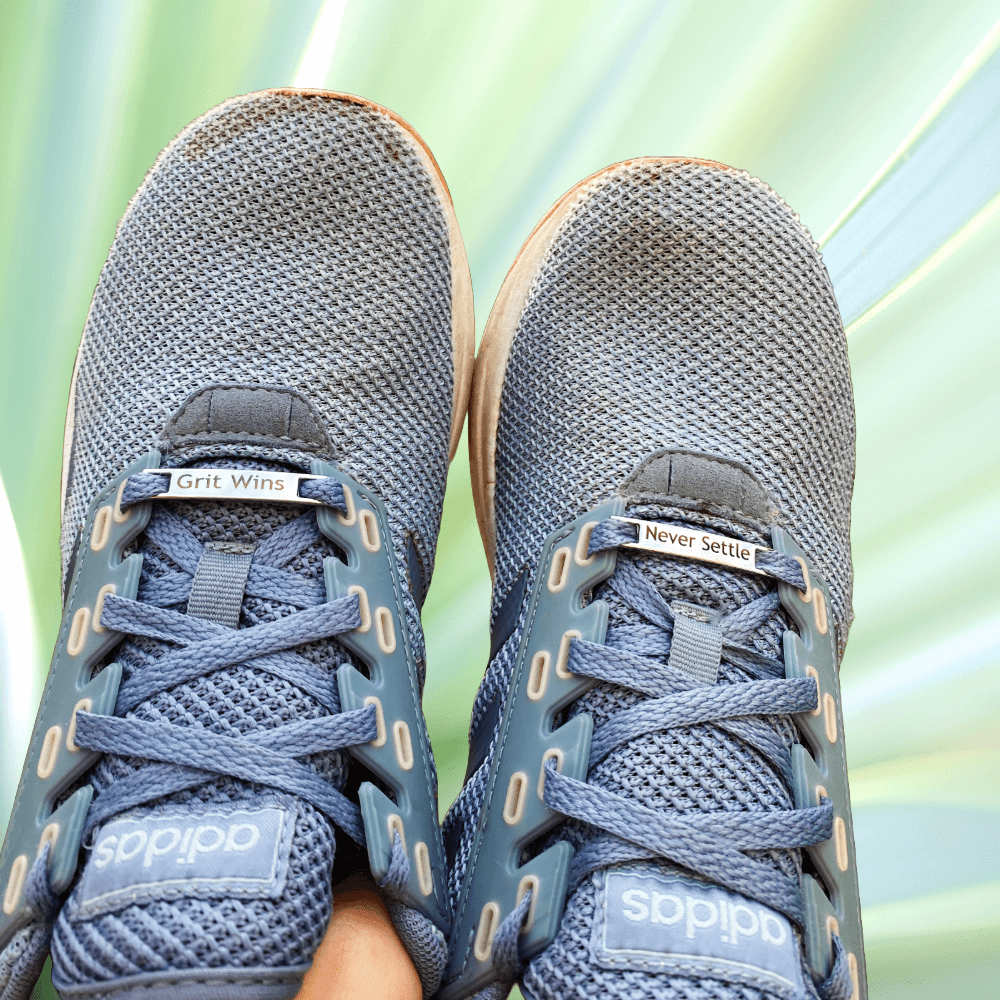 Image of running shoes with the Tags Grit Wins Never Settle laced onto the laces.
