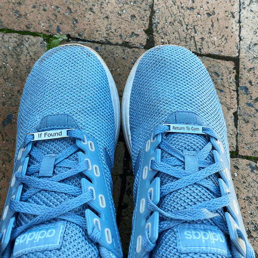 Image of etched shoe tags If Found Return To gym on a pair of running shoes on bricks