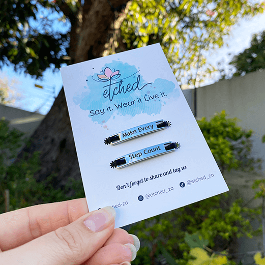 Image of etched product card showing the Make Every Step Count shoe tags being held up by a hand with a tree in the background