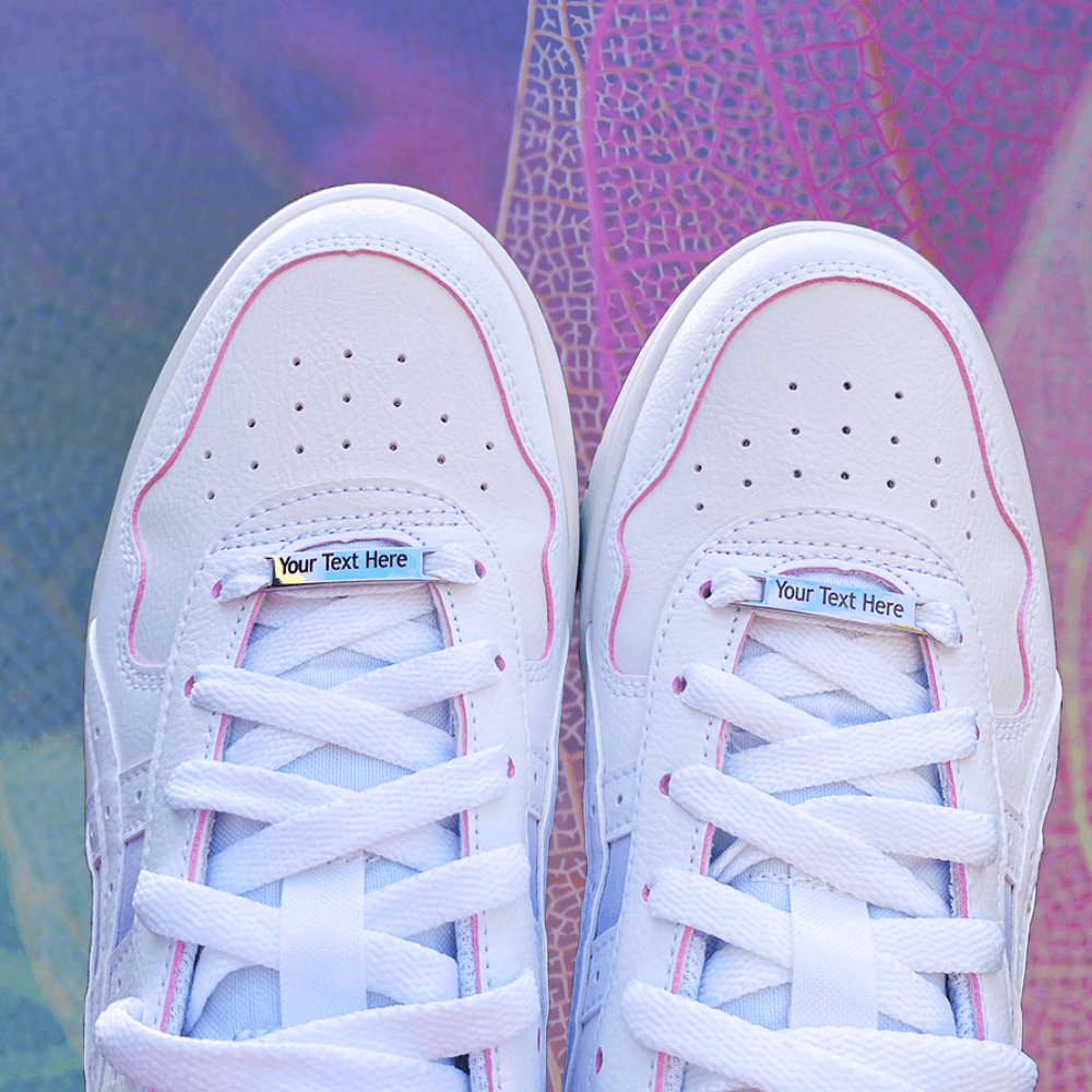 Image of etched shoe tags saying Your Text here on a pair of shoes on a pink and purple textured background background